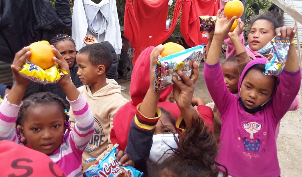 A group of children in an informal settlement holding snacks.